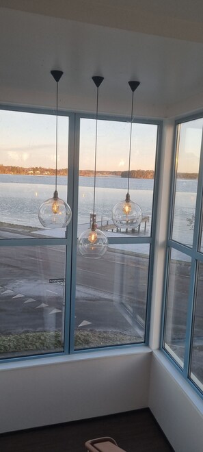 A room with large windows overlooking a body of water, featuring three hanging light fixtures. - Hotell Wettern (Karlsborg)