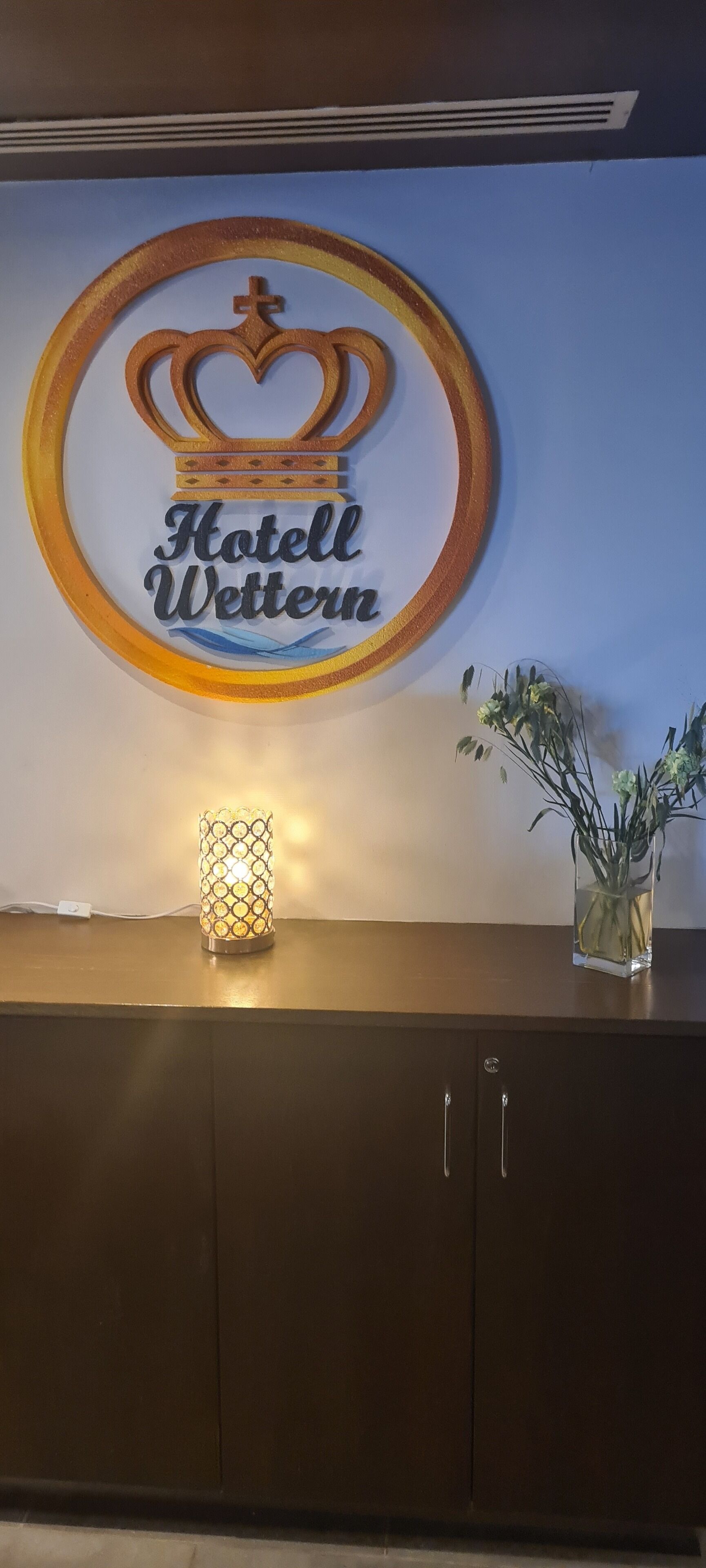 A wall-mounted sign for 'Hotel Wettern' with a crown symbol, a lit candle, and a vase with plants.
