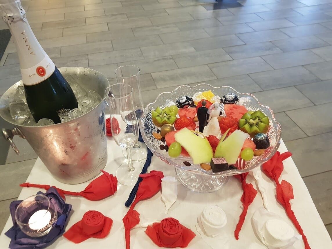 Ett bord med en flaska champagne, glas, en fruktfat och dekorationer i form av röda rosor.
