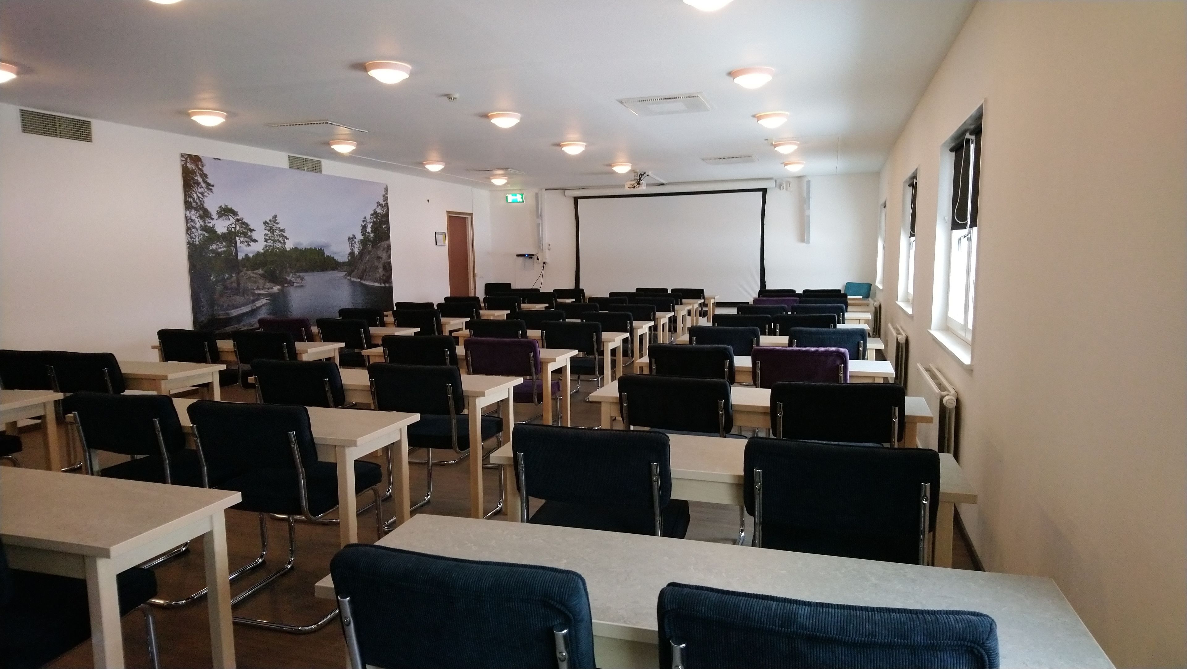 A classroom with rows of desks and chairs, a projector screen, and a large mural on the wall.