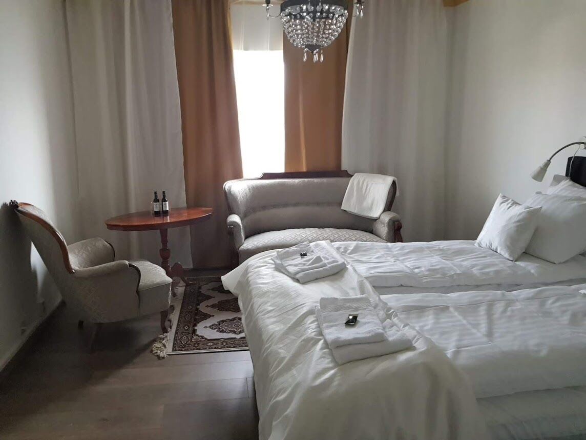 A hotel room with a large bed, a chair, a small table, and a chandelier.