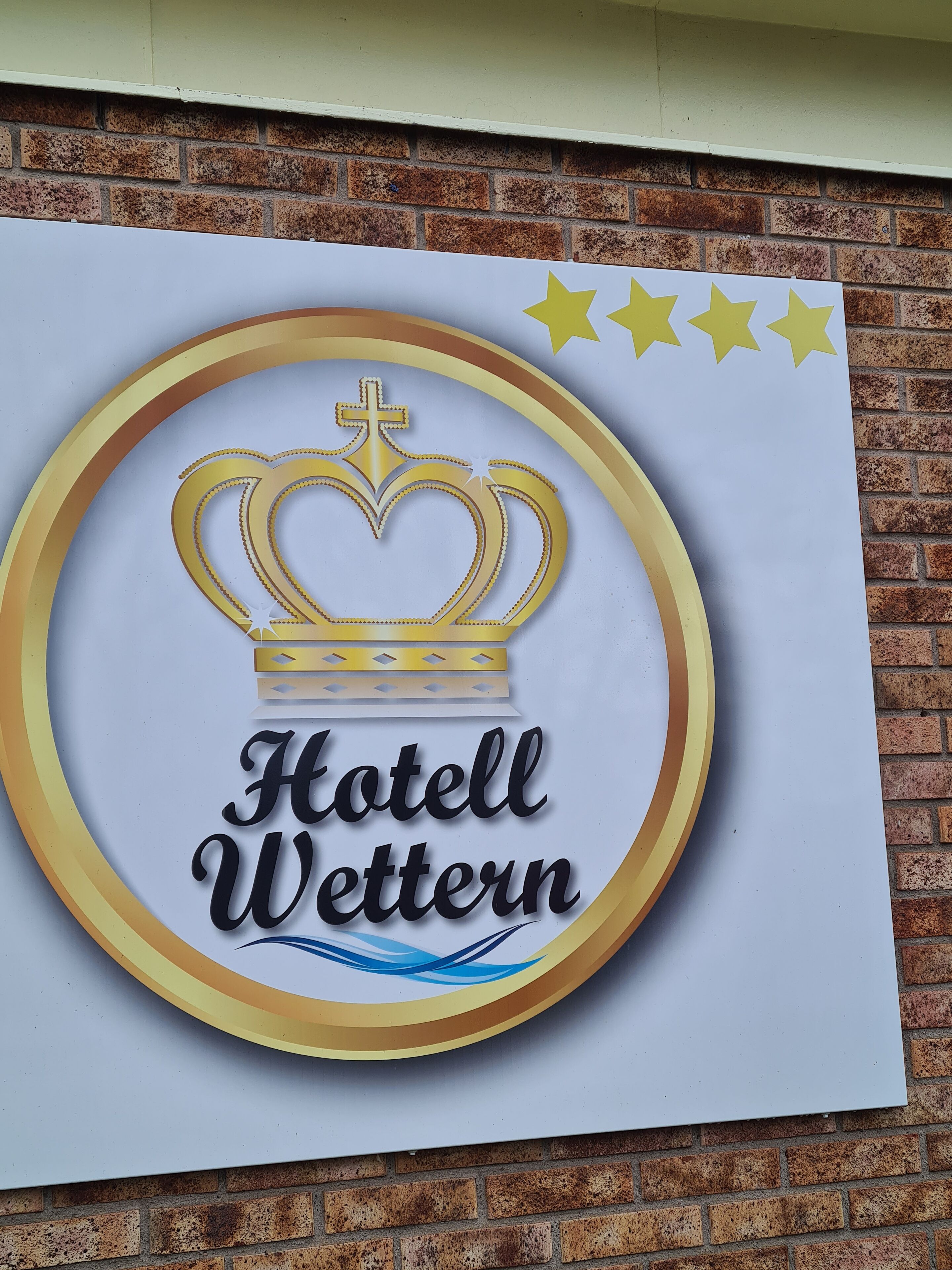 En skylt med en kronlogotyp och texten ”Hotel Wetten” på en tegelvägg.