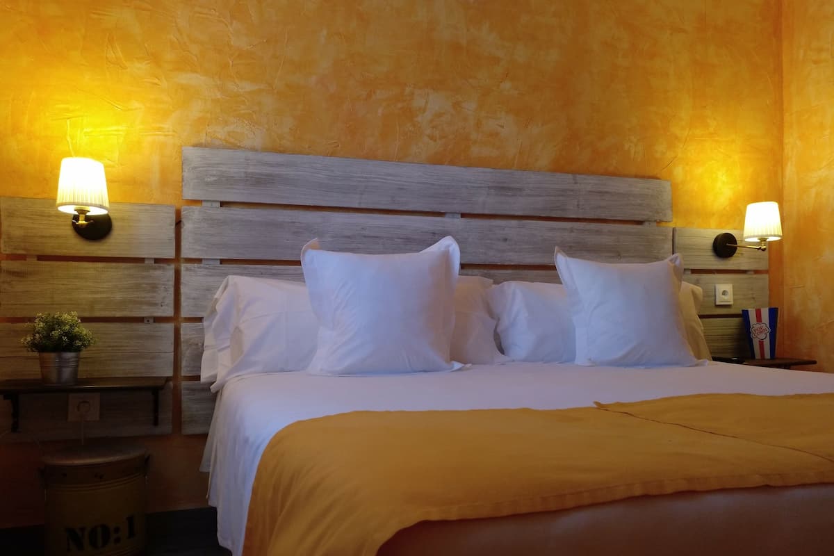 A hotel room with a wooden headboard, white bedding, and two wall-mounted lamps.
