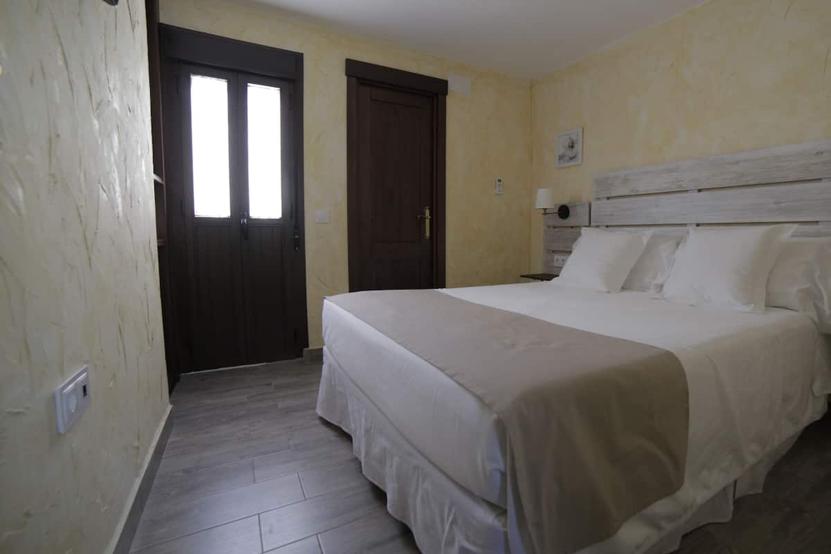 A bedroom with a bed, a nightstand, a lamp, a door, and a small stool.