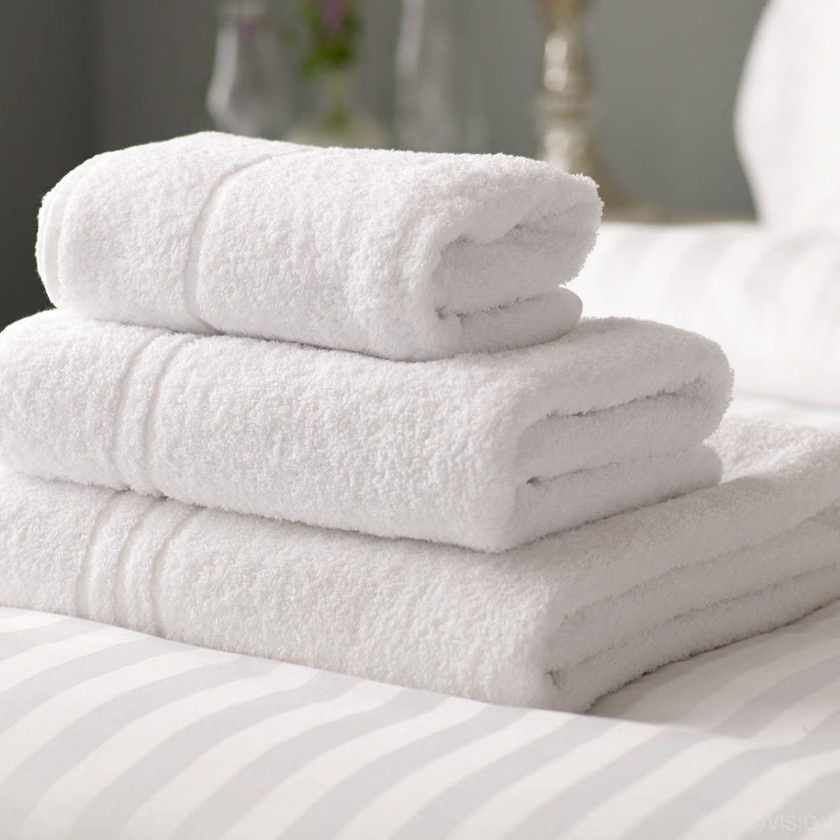 A stack of white towels on a bed with striped bedding.