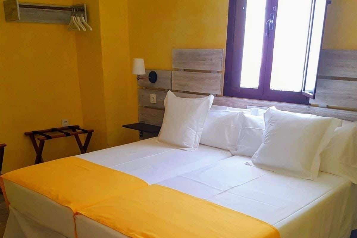 A large bed with a white and orange bedspread, a wooden headboard, and a nightstand with a lamp.