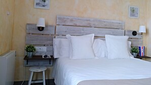 Un dormitorio con cabecera de madera, ropa de cama blanca, dos mesitas de noche con lámparas y una pequeña planta en maceta sobre una de ellas.