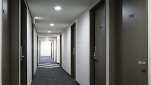 A long, narrow hotel corridor with carpeted floors and doors on both sides, leading to individual rooms.