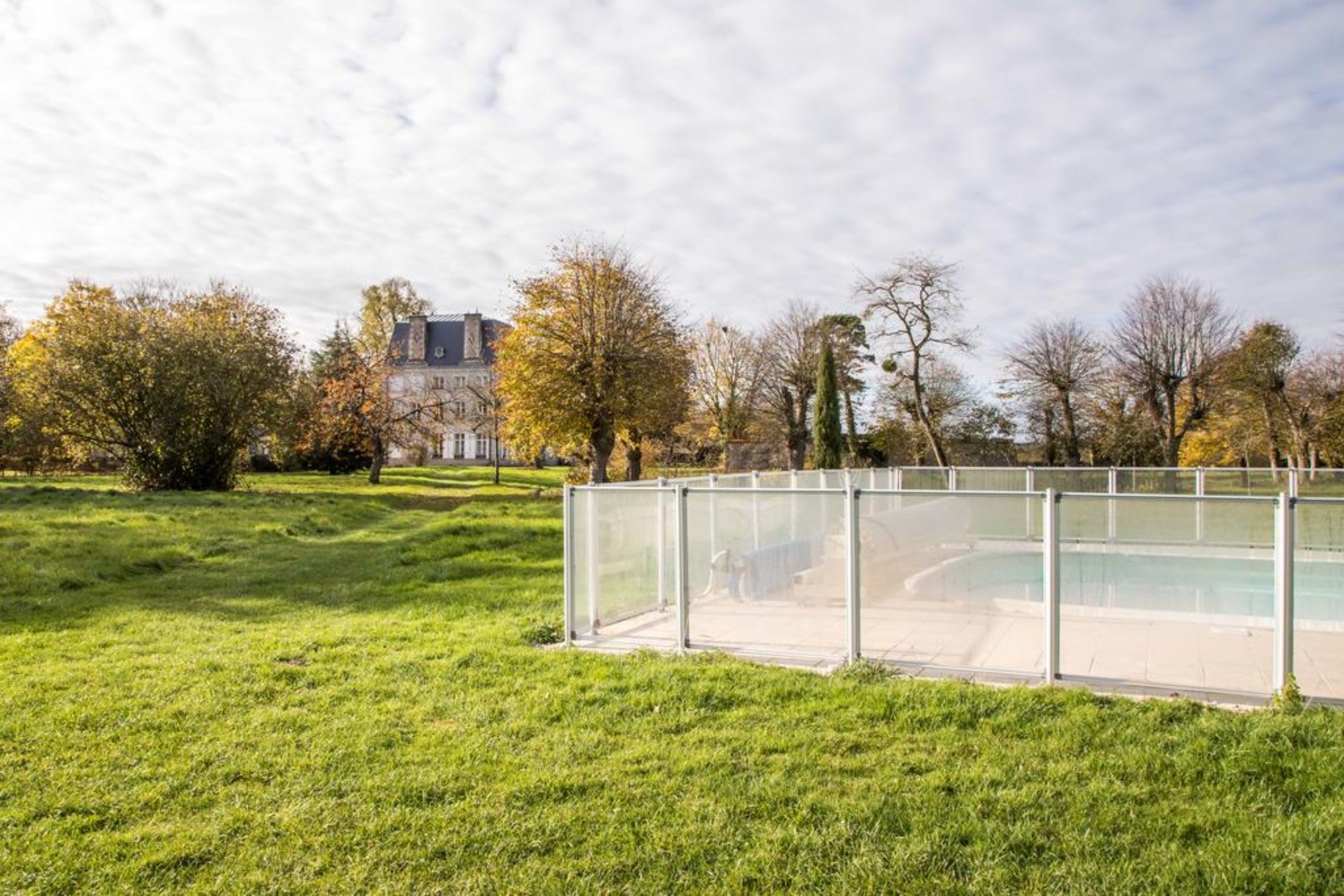 A grassy area with a glass-enclosed pool and a building in the background.