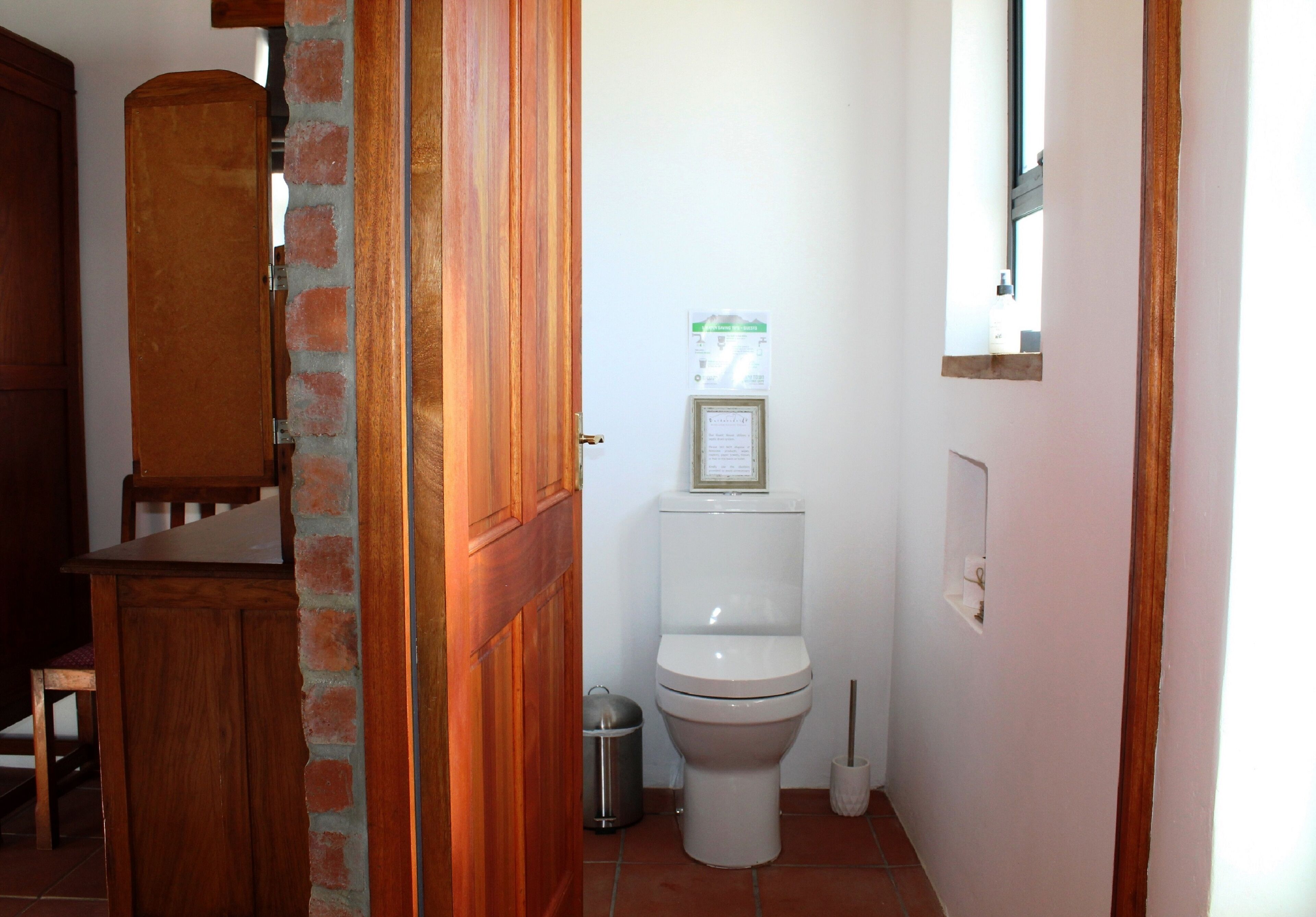 A small bathroom with a toilet, a trash can, and a wooden cabinet.