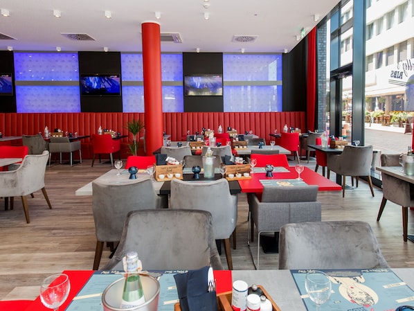 Un restaurante con sillas rojas y grises, mesas con menús y un grueso pilar rojo.