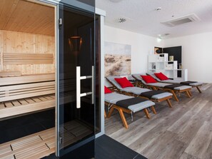 A modern spa room with wooden floors, glass doors, and multiple sun loungers with red cushions. - DORMERO Hotel Salzgitter (Salzgitter)