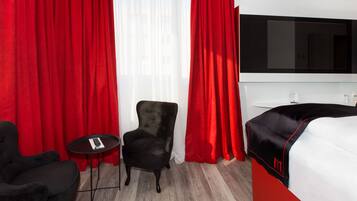 A hotel room with a bed, a TV, a black armchair, and a small table.