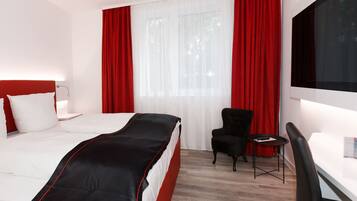 A hotel room with a bed, a desk, a chair, and a large window with red curtains.