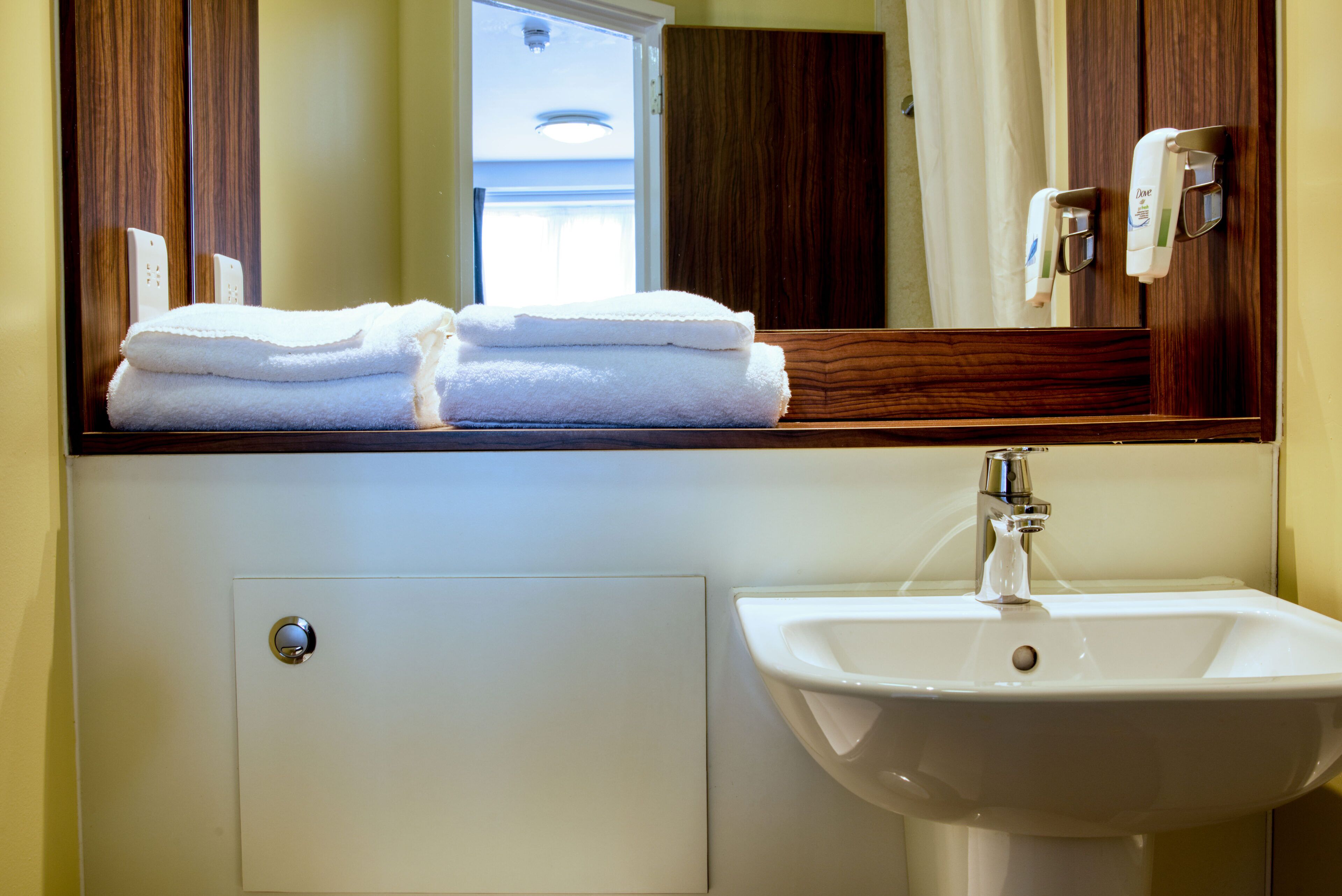 A bathroom with a sink, mirror, and stacked towels.