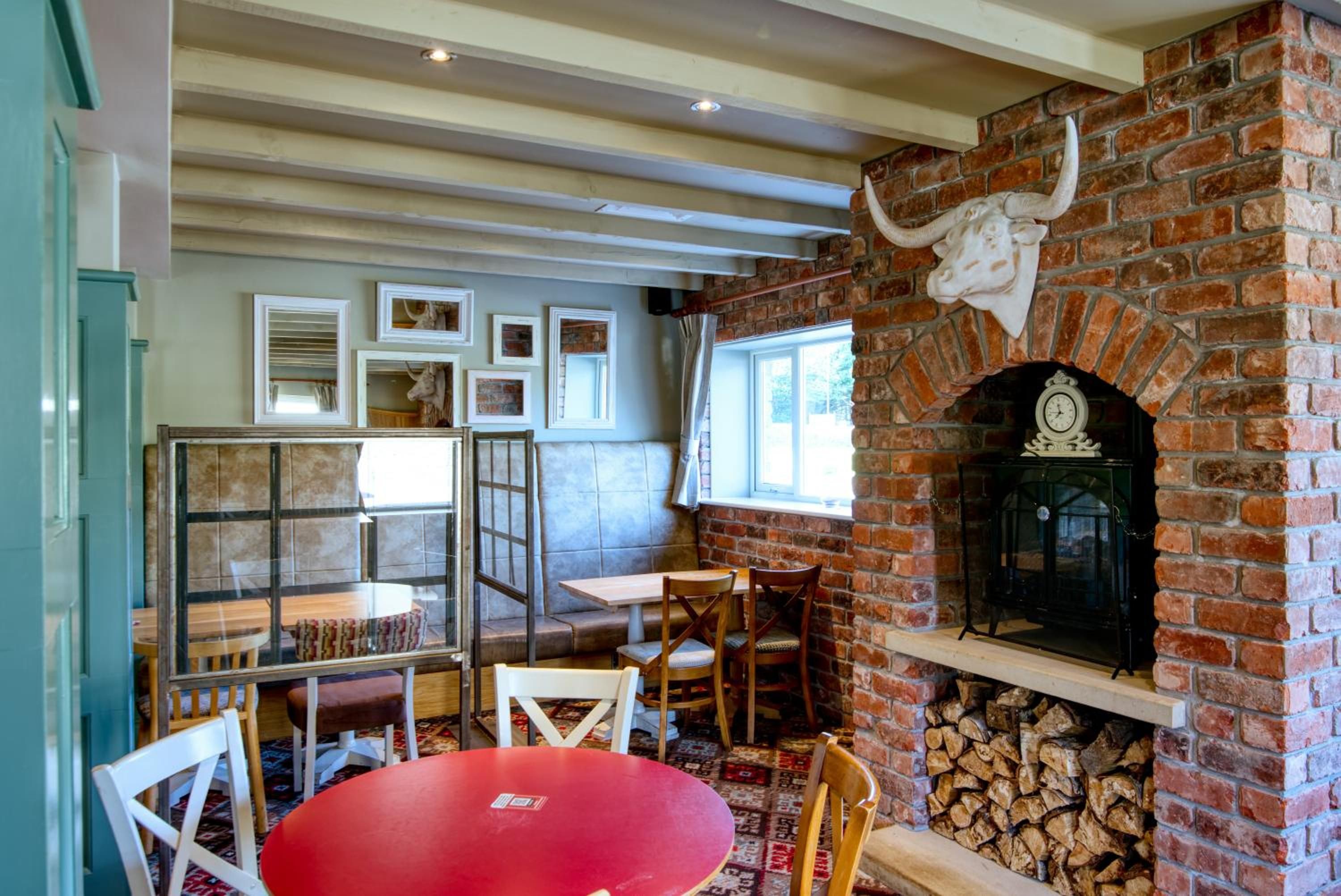 A cozy interior with a brick fireplace, wooden furniture, and framed artwork on the walls.