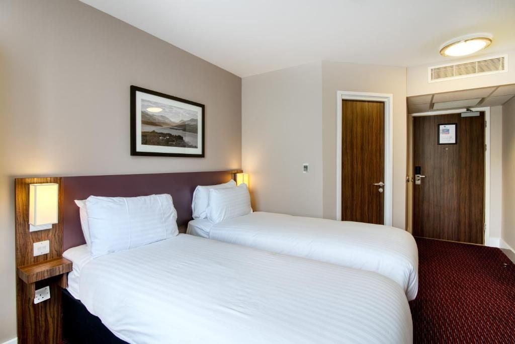 A hotel room with two beds, a framed picture on the wall, and a door with a sign.