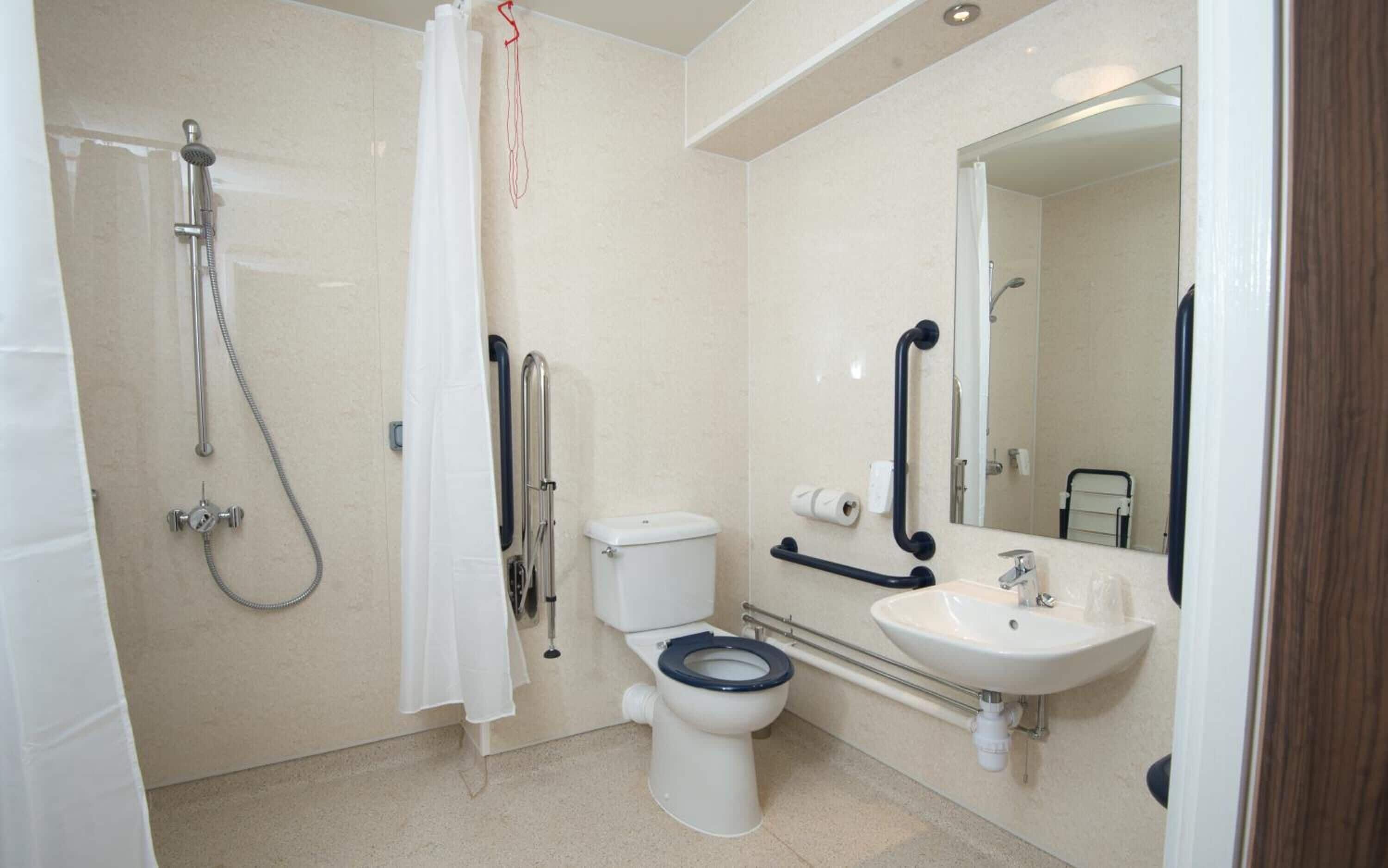 A bathroom with a shower, toilet, sink, and mirror.
