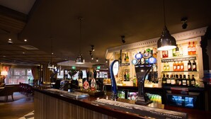 Zona de bar con suelo de cuadros, paneles de madera y una variedad de botellas y vasos en estantes.