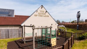 Un parque infantil con estructuras para escalar y una casita de juegos con el letrero 'The Queen of the Loch'.