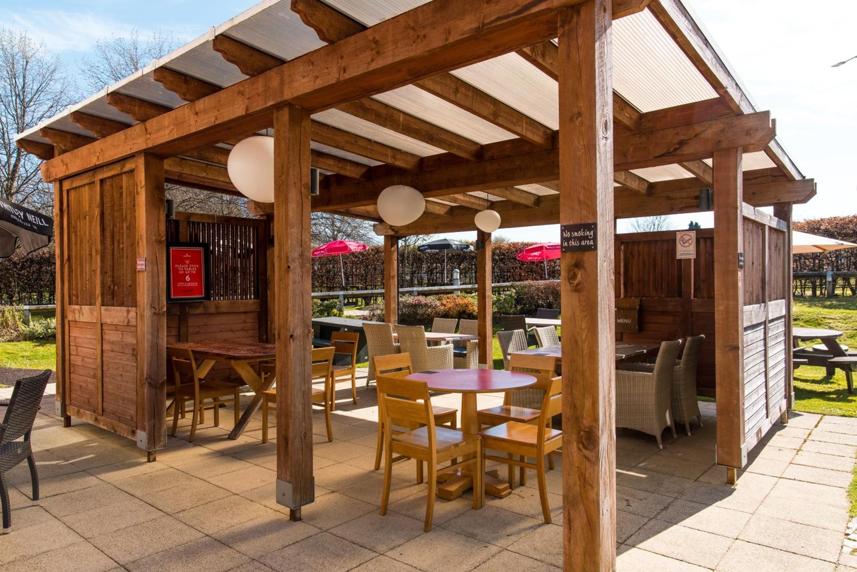 An outdoor seating area with wooden tables and chairs, a covered section with a sign, and a menu board.