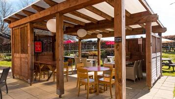 An outdoor seating area with wooden tables and chairs, a covered section with a sign, and a menu board.