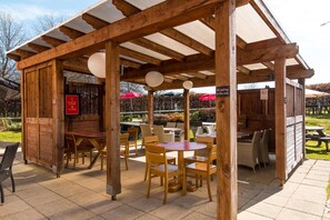 An outdoor seating area with wooden tables and chairs, a covered section with a sign, and a menu board.