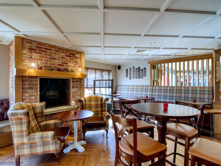 Interior acogedor de restaurante con chimenea de ladrillo, mobiliario a cuadros y techo de madera.