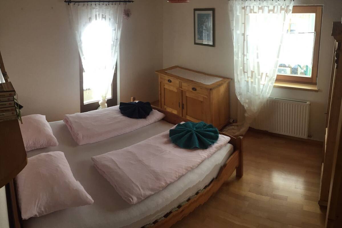 Un dormitorio con dos camas individuales, un aparador de madera, un radiador y una ventana con cortinas.
