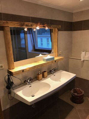 A bathroom with a large mirror, two sinks, wooden shelves, and a window with blinds. - Tuxie Haus (Tux)