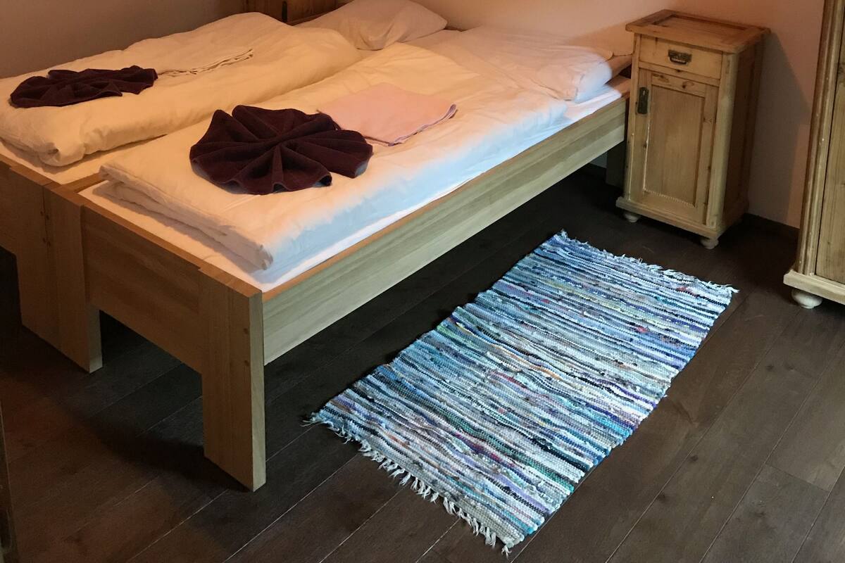 Un dormitorio con una cama de madera, una mesita de noche pequeña, una pared de ladrillo y una lámpara colgante.
