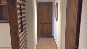 A narrow hallway with a wooden door on the right, a wooden wall with a hanging coat rack on the left, and a tiled floor. - Tuxie Haus (Tux)