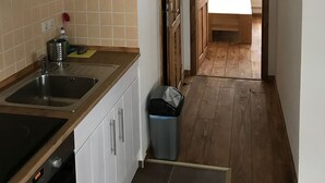 A narrow kitchen with white cabinets, a wooden ceiling, and a view into a bedroom through a doorway. - Tuxie Haus (Tux)