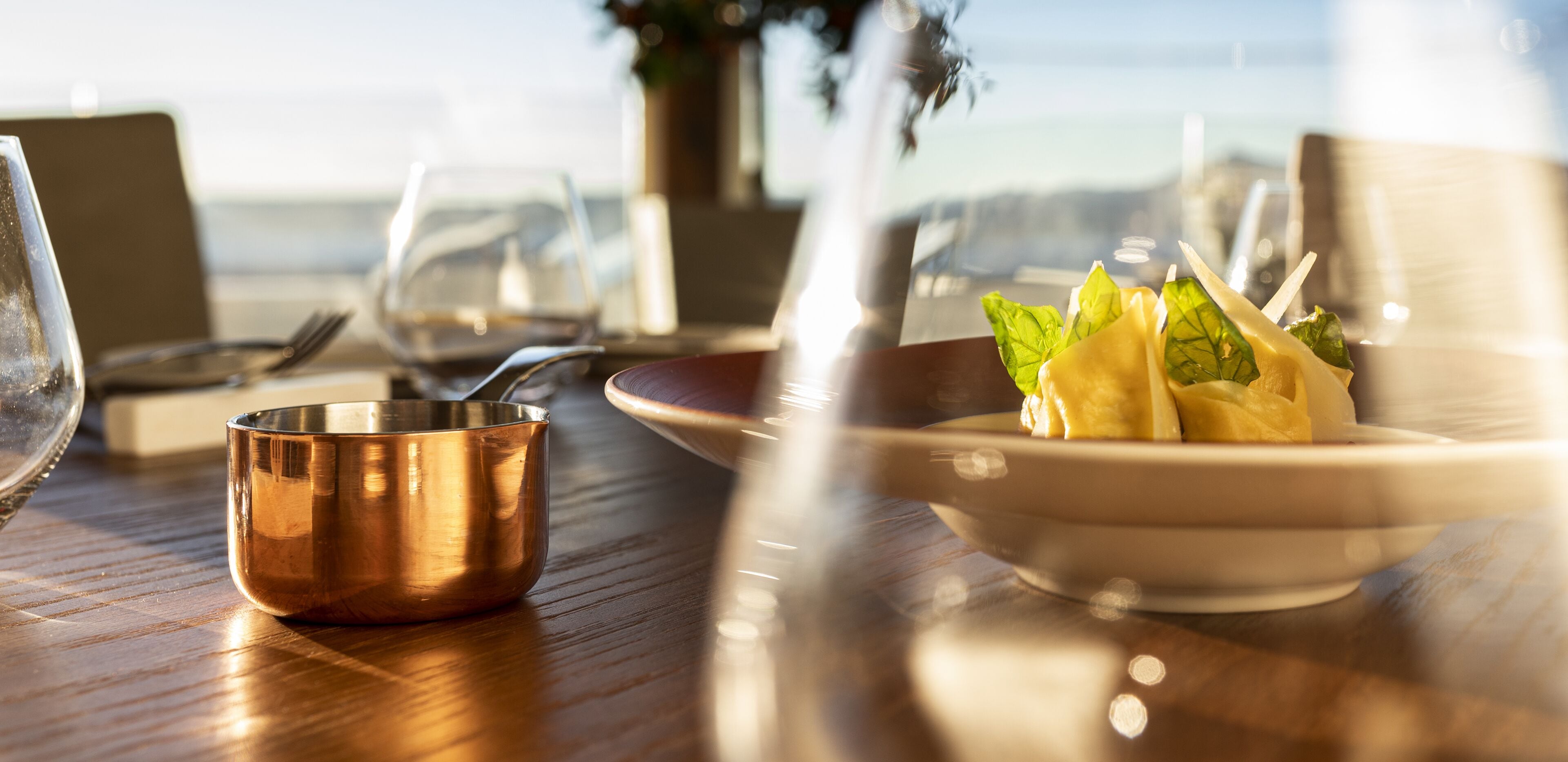 A dining table with a copper bowl, a plate with food, and wine glasses.