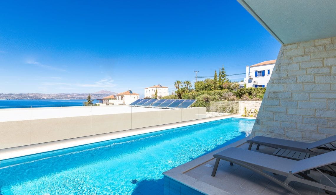Una piscina con vista despejada al mar, una silla de descanso y paneles solares en el techo.