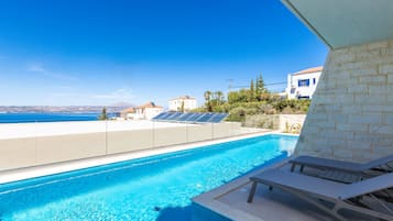 Una piscina con vista despejada al mar, una silla de descanso y paneles solares en el techo.