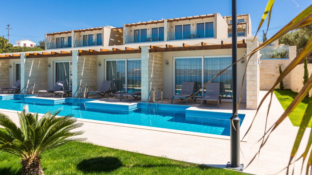 A modern hotel with a pool area, multiple lounge chairs, and a well-maintained garden.