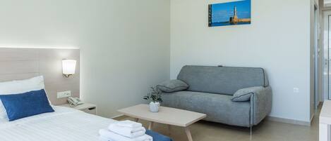 Une chambre d’hôtel avec un lit, un canapé gris, une petite table avec un vase et un tableau au mur.
