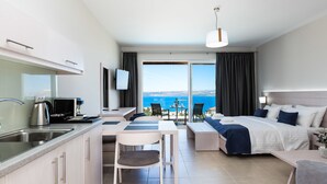 A modern hotel room with a kitchenette, a dining area, a bed with a view, and a large window. - Sun and Sea Plus Resort Hotel (Apokoronas)