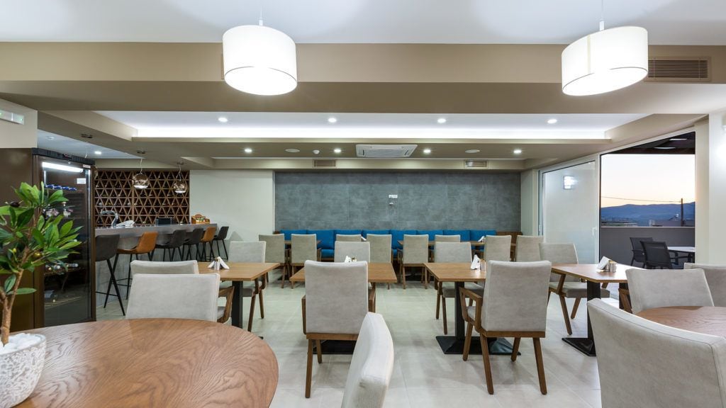 Una sala de conferencias moderna con mesas y sillas redondas, un área de cocina y un ventanal con vistas.