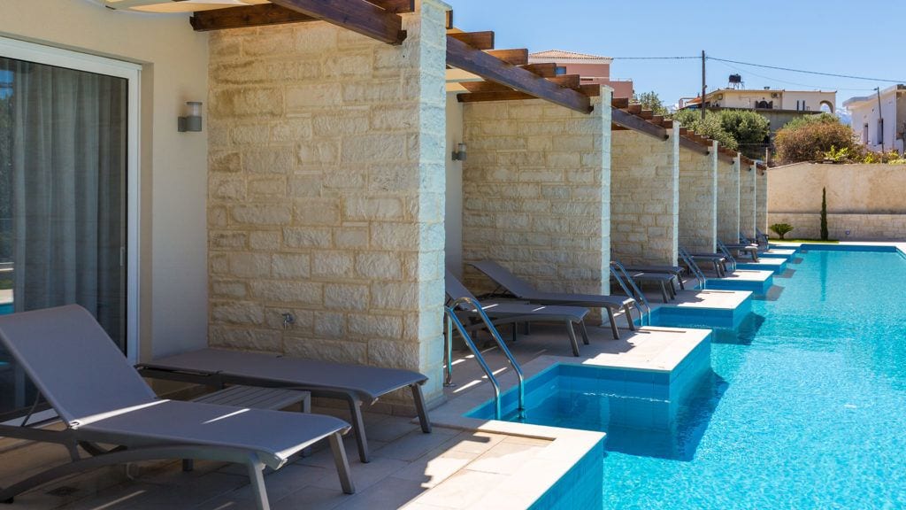 Piscina com cadeiras de espreguiçadeira e uma parede de pedra.