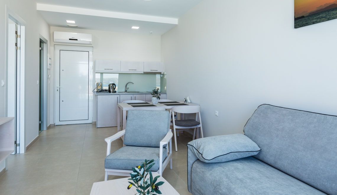 A modern living room with a grey sofa, a small table with a plant, and a kitchen in the background.