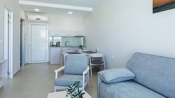 A modern living room with a grey sofa, a small table with a plant, and a kitchen in the background.