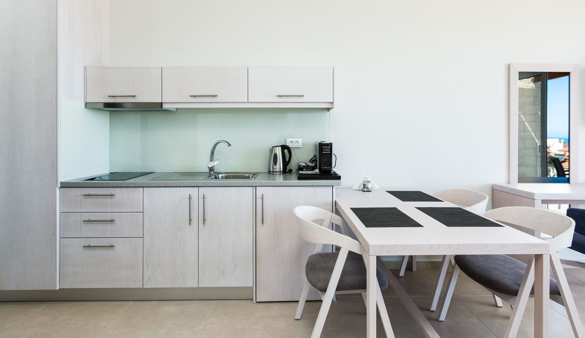 Una cocina moderna con armarios blancos, un lavamanos de acero inoxidable y una cafetera. Hay una mesa de comedor con cuatro sillas.