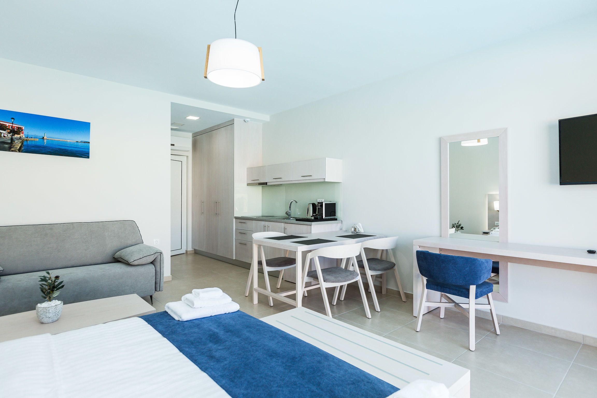 Una habitación de hotel moderna con cama, escritorio, silla, sofá, mesa de comedor y kitchenette.