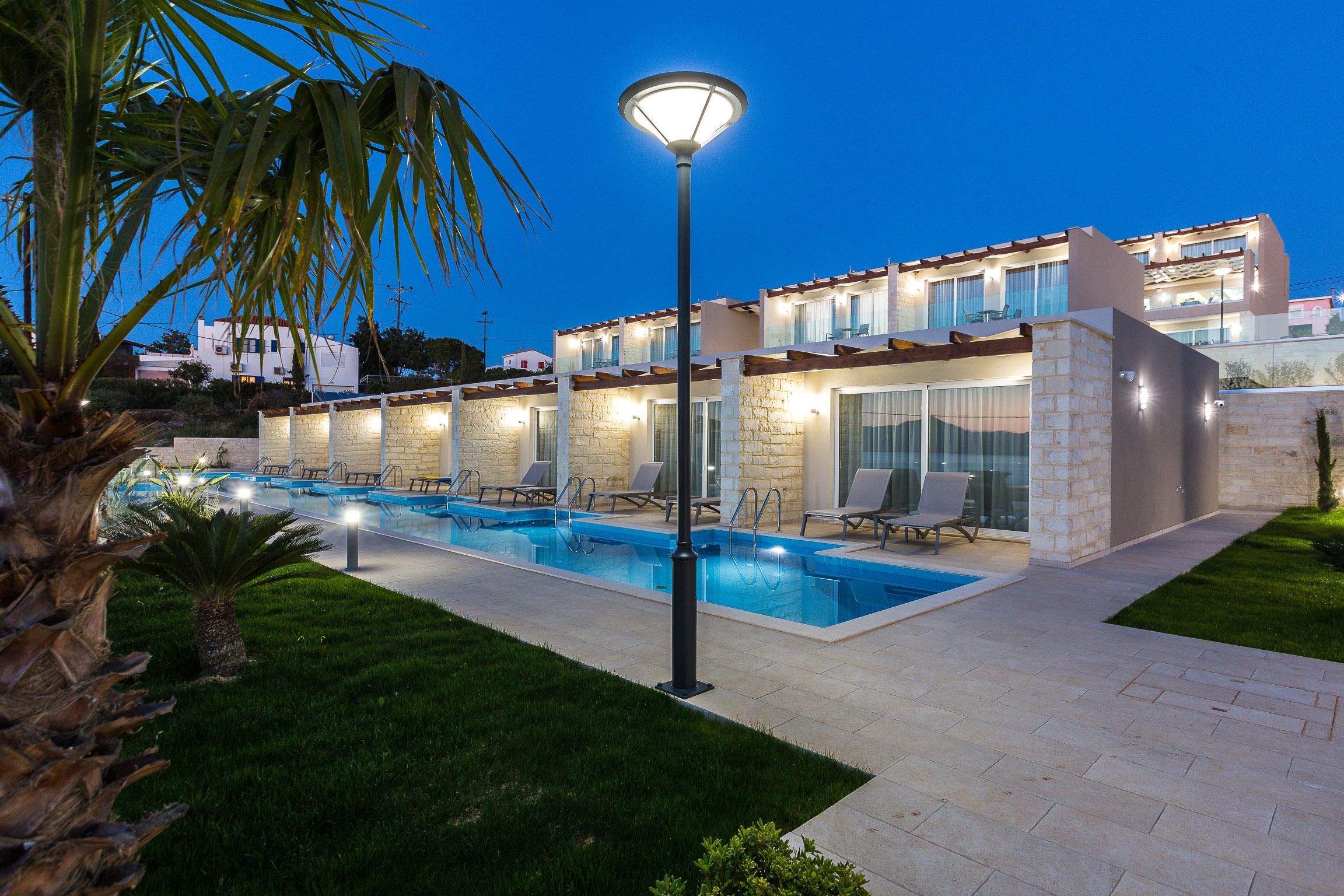 A modern hotel with a swimming pool, outdoor seating, and a well-lit facade.