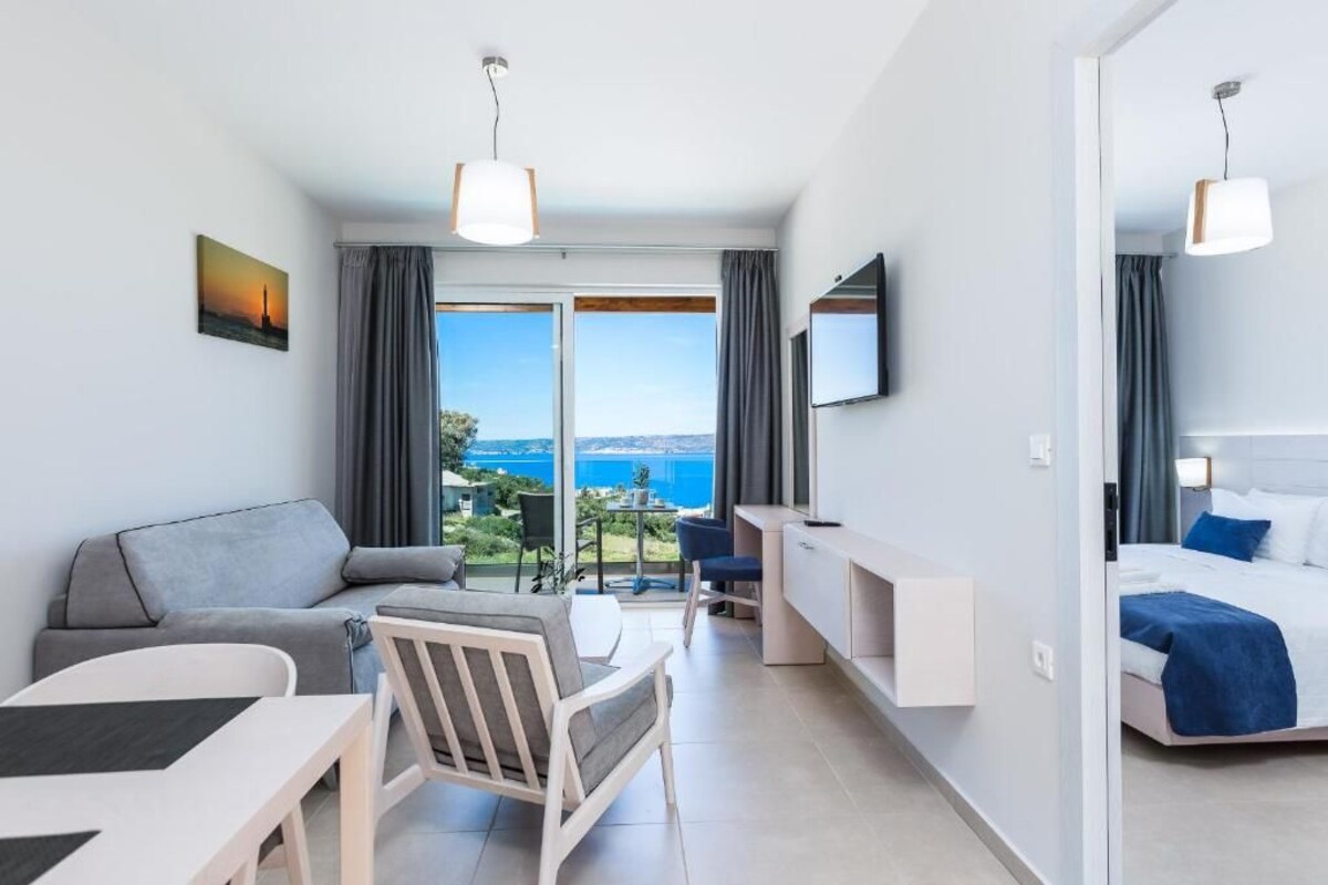 A modern hotel room with a balcony, a sofa, a desk, and a bed.