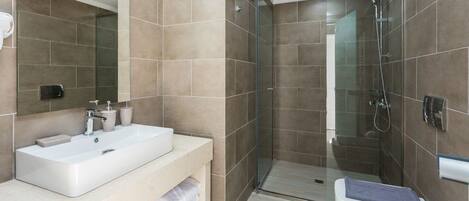 Un baño moderno con un lavabo grande, espejo y cabina de ducha de vidrio.