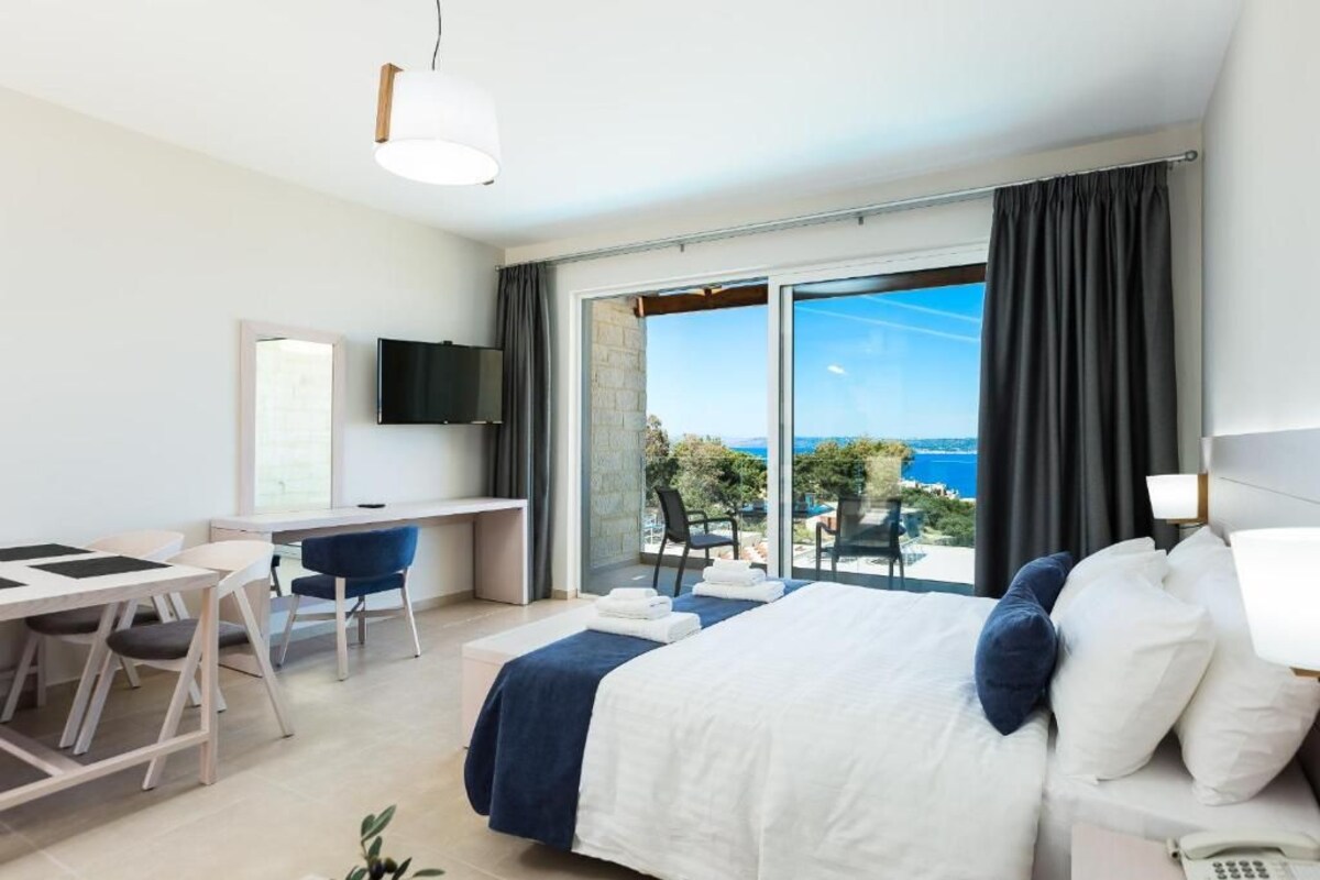 A hotel room with a bed, a desk, a chair, a TV, and a balcony with a view.