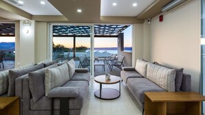 A modern living room with a sofa set, a coffee table, and a view through a glass door to an outdoor patio area. - Sun and Sea Plus Resort Hotel (Apokoronas)